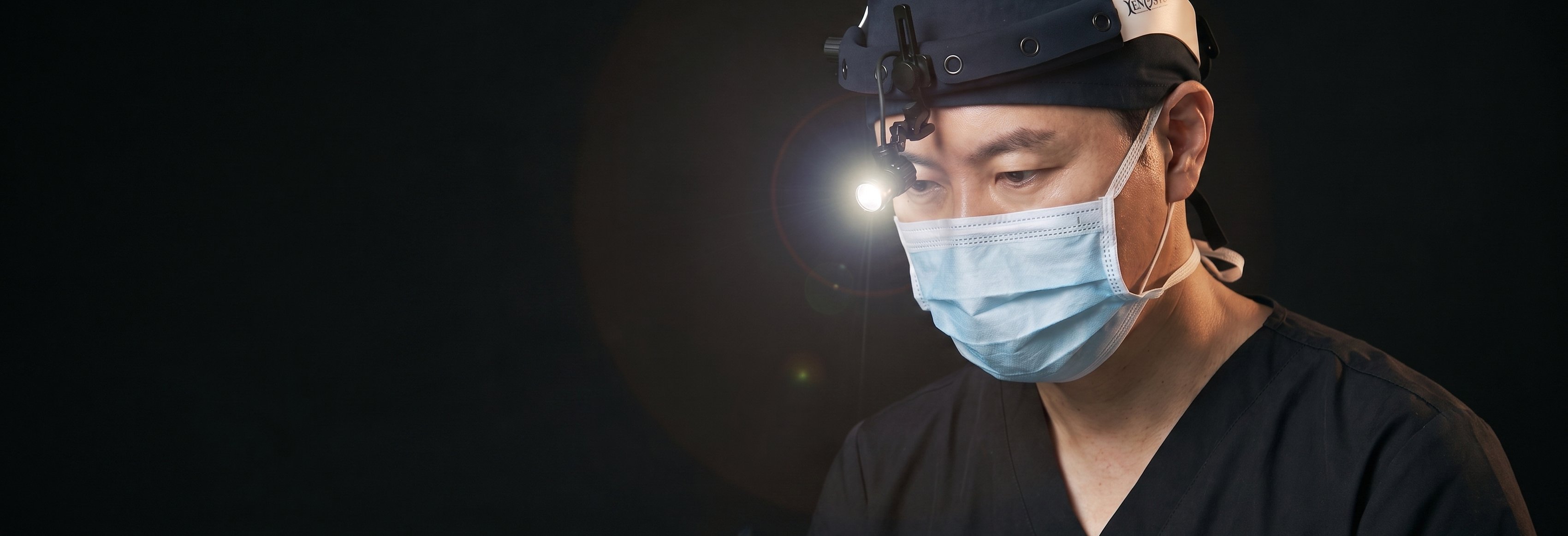 นพ. คิม อึยกอน แห่ง UNE Plastic Surgery สวมไฟส่องผ่าตัดและจดจ่อกับบริเวณผ่าตัด